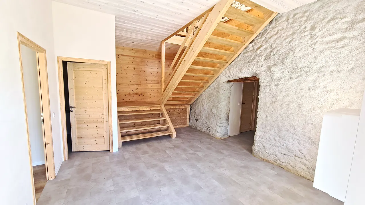 Grand hall d'accueil avec escalier en bois et mur en pierre chaulée